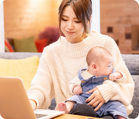 子どもを抱きながらパソコンを見る女性